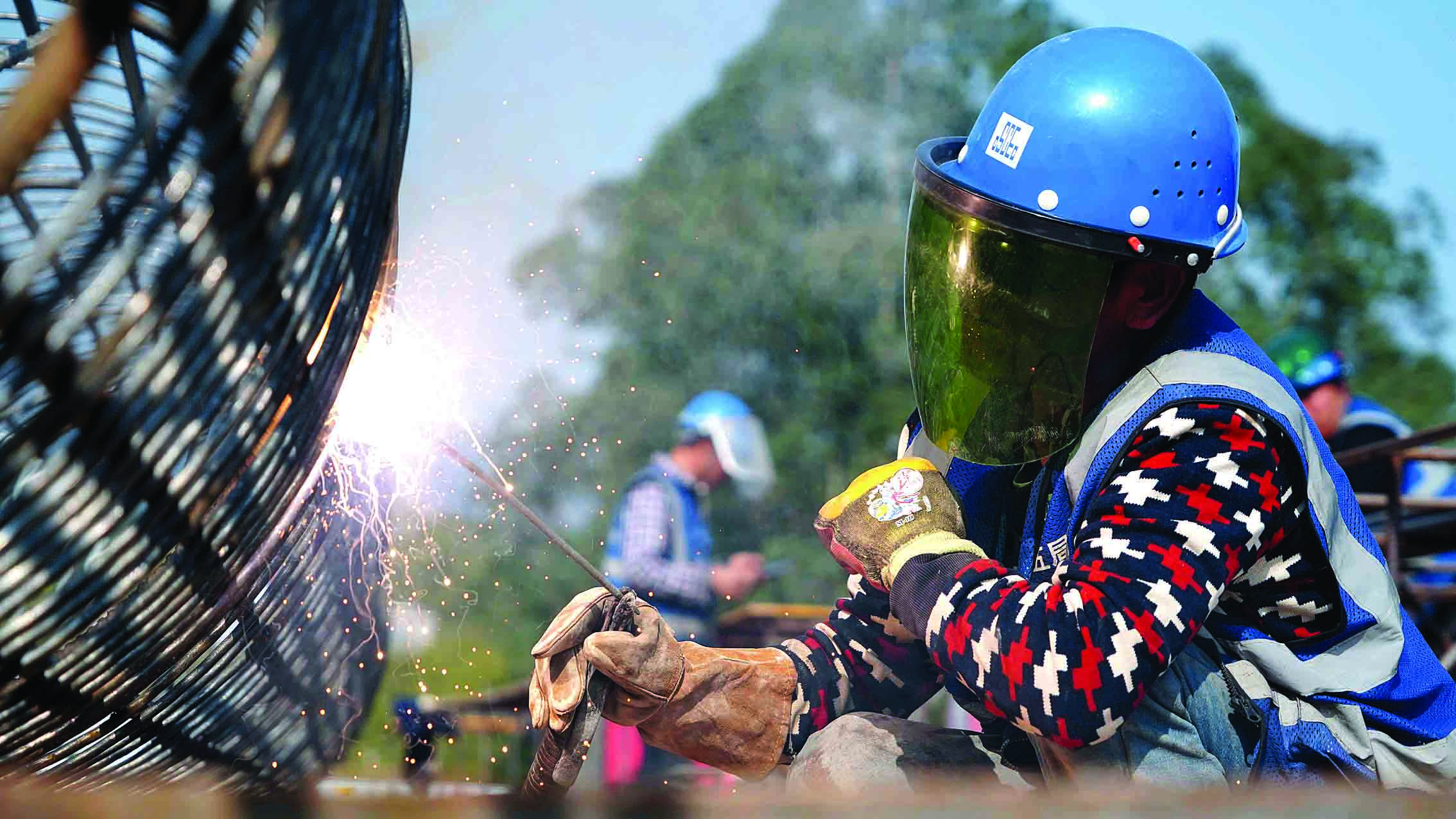     县道219线龙华路段桥梁施工现场，工人在焊接钢筋笼。