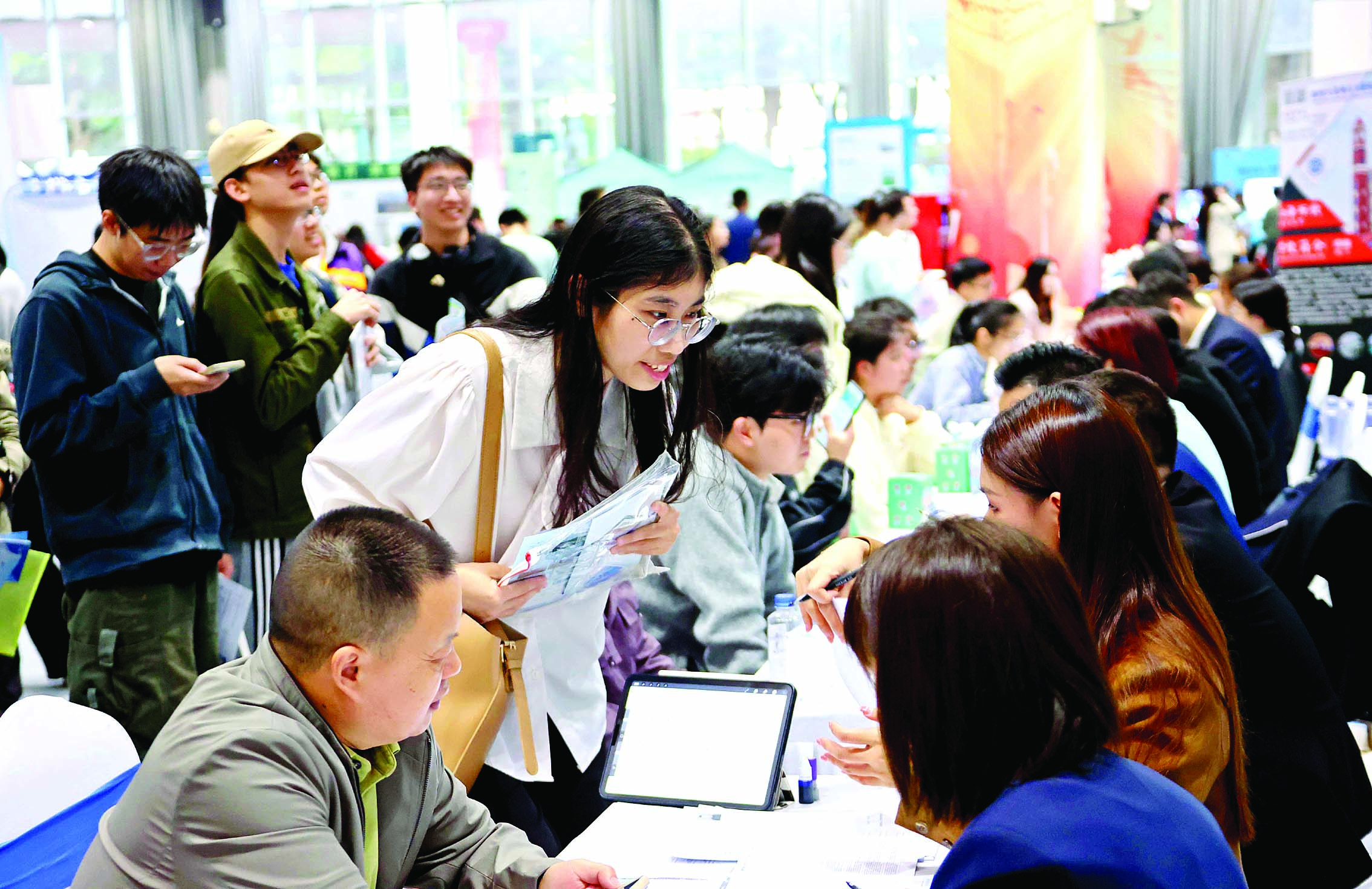     求职者携带简历在展位前与招聘人员交流。