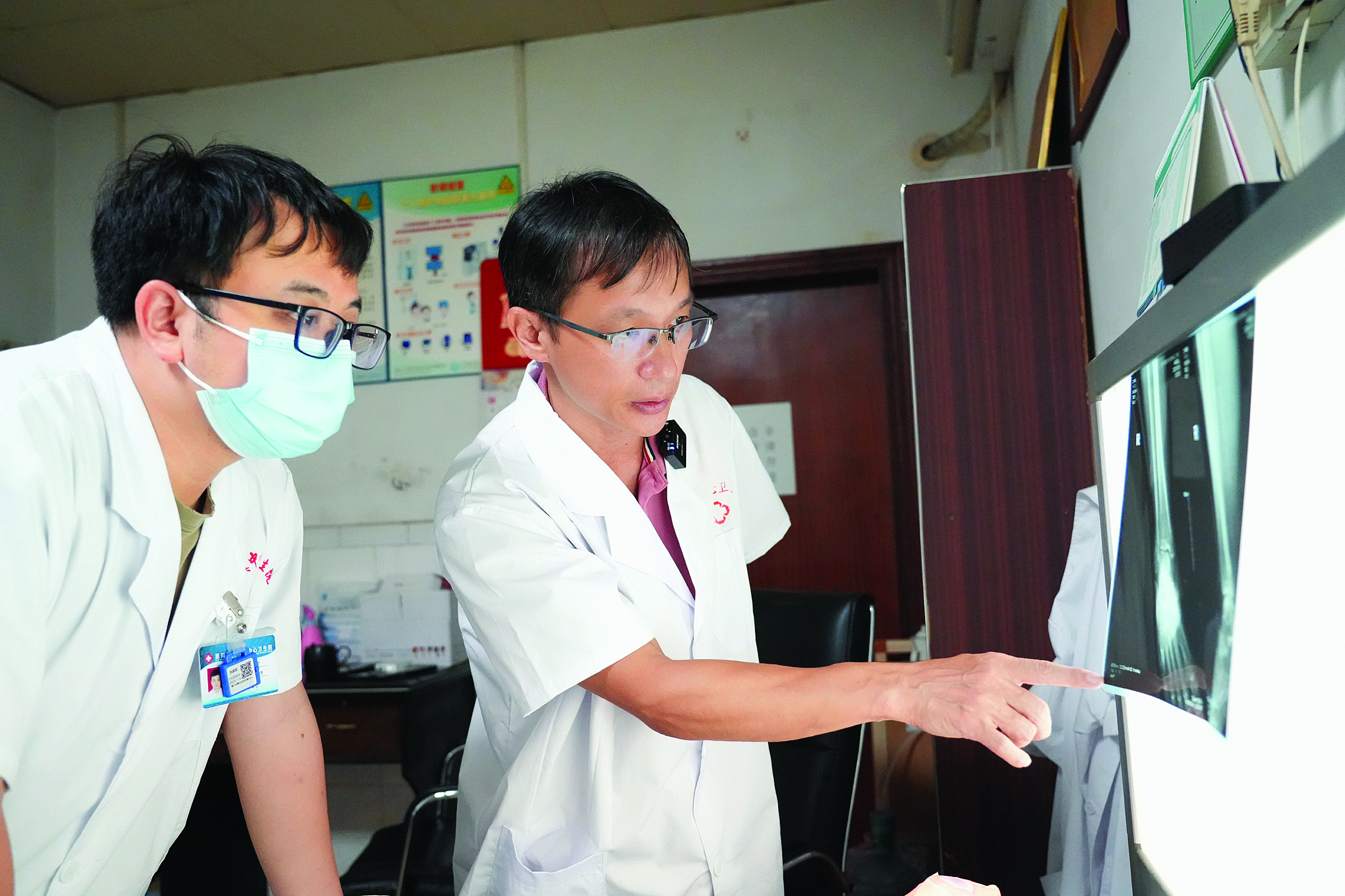     吴世祥（右）指导新圩镇中心卫生院放射科医生进行影像诊断。    惠州日报记者许文昌 摄