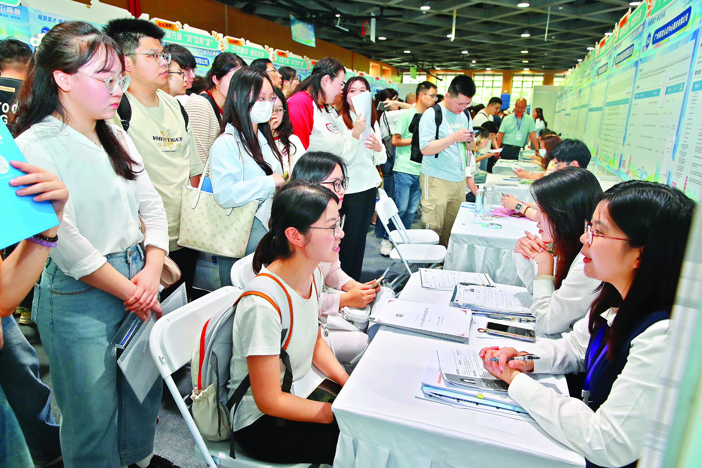     “百万英才汇南粤”2025年N城联动春季招聘活动（武汉站）现场，求职者在企业摊位前咨询交流。