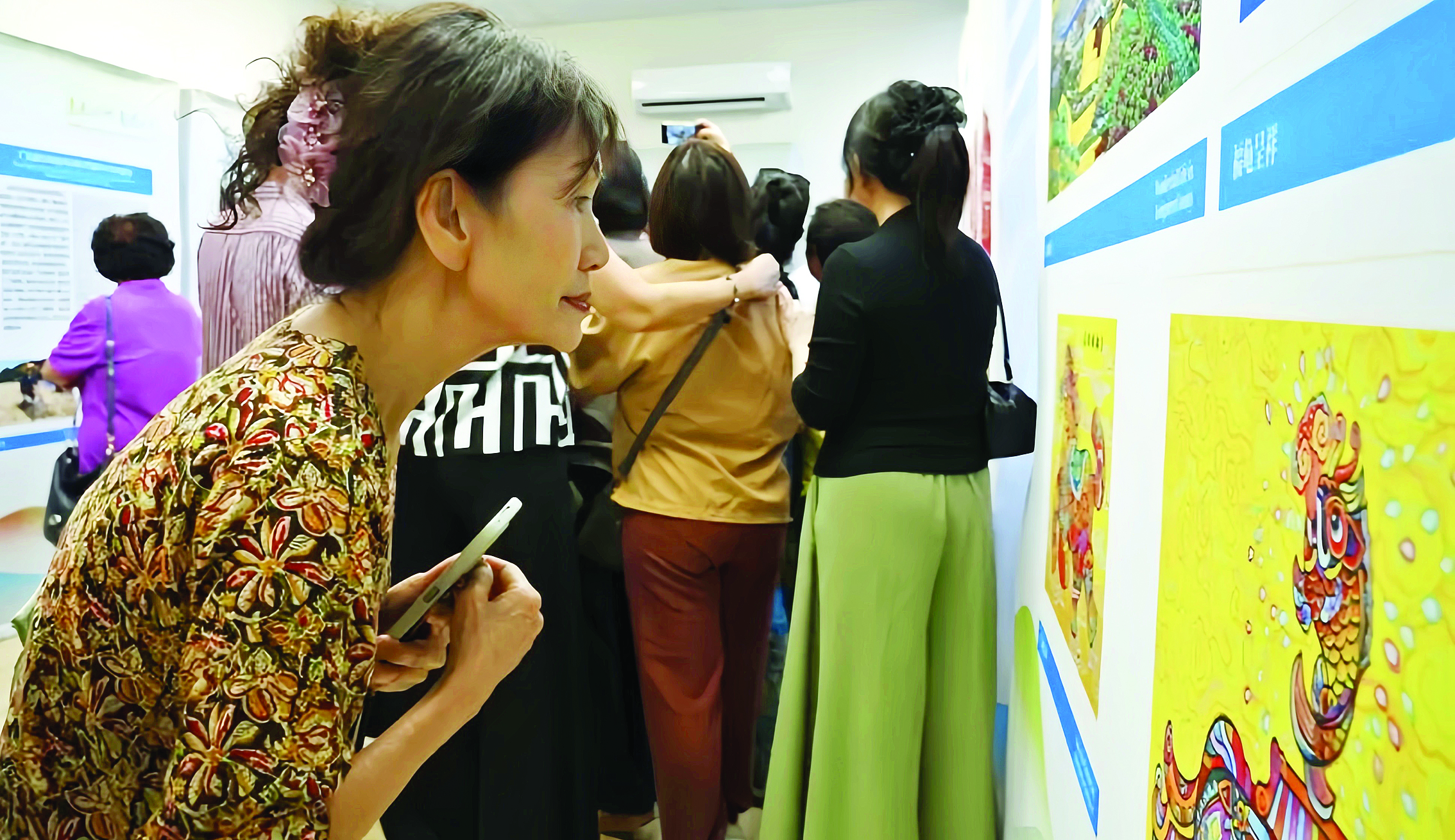     游客俯身欣赏龙门农民画。    惠州日报记者黄宇翔 通讯员龙旅宣 摄